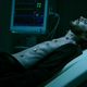 Morbius, looking pale and sickly, lies shirtless on a hospital bed next to a heart rate monitor.